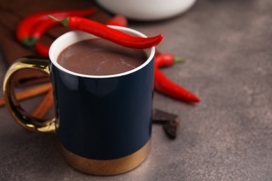 Photo of Cup of hot chocolate with chili pepper on grey table. Space for text