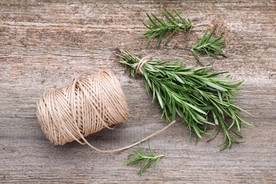 Sprigs of fresh rosemary and twine on wooden table, flat lay