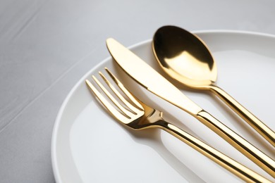 Photo of Plate with golden cutlery on grey table, closeup