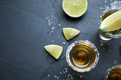Mexican Tequila shots with salt and lime slices on grey table, flat lay. Space for text