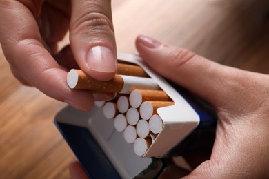 Woman taking cigarette out of pack at wooden table, closeup