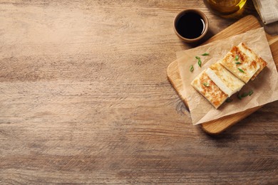 Delicious turnip cake with green onion and soy sauce on wooden table, flat lay. Space for text