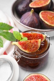Glass jar of tasty sweet fig jam and fruits on white tiled table