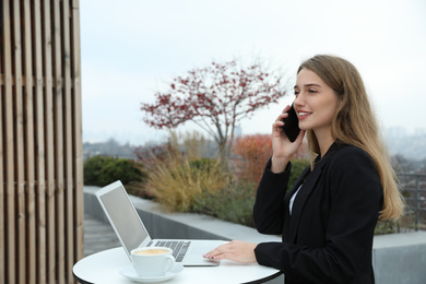 Photo of Businesswoman with laptop talking on phone in outdoor cafe. Corporate blog