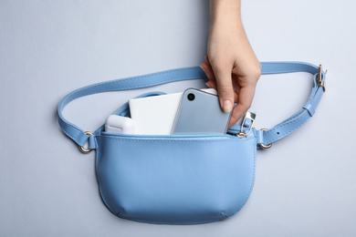 Woman taking smartphone from small bag on light grey background, top view