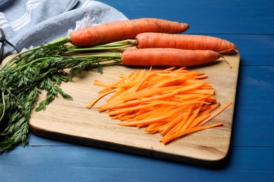 Fresh ripe juicy carrot sticks and whole vegetables on blue wooden table