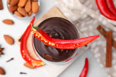 Photo of Glass of hot chocolate with chili pepper on white table, flat lay
