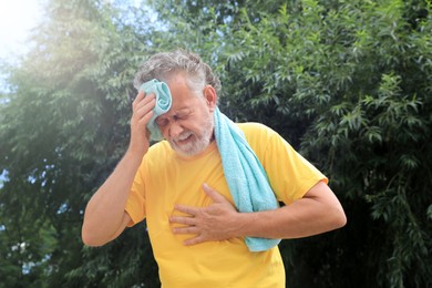 Senior man with towel suffering from heat stroke outdoors