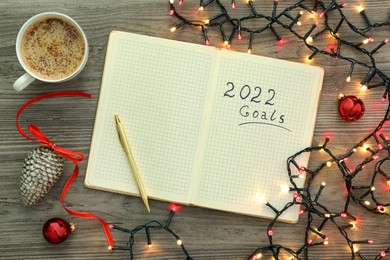 Inscription 2022 Goals written in planner, cup of coffee and Christmas decor on wooden background, flat lay. New Year aims