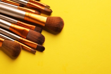 Different makeup brushes on yellow background, closeup. Space for text