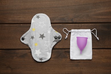 Reusable cloth pad and menstrual cup on wooden table, flat lay