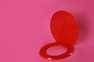 New red plastic toilet seat on pink background, space for text