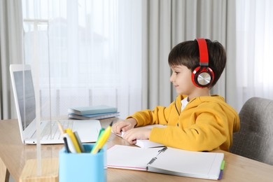 Cute little boy with modern laptop studying online at home. E-learning