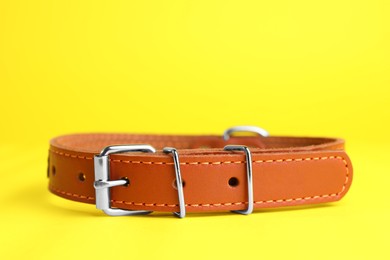 Photo of Brown leather dog collar on yellow background, closeup. Space for text