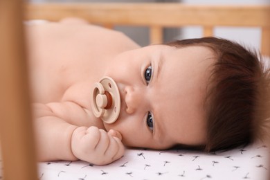 Cute little baby with pacifier lying in comfortable crib, closeup. Bedtime