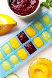 Different purees in ice cube tray and ingredients on white table, flat lay. Ready for freezing