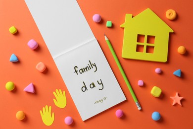 Happy Family Day. Flat lay composition with notebook and house model on orange background