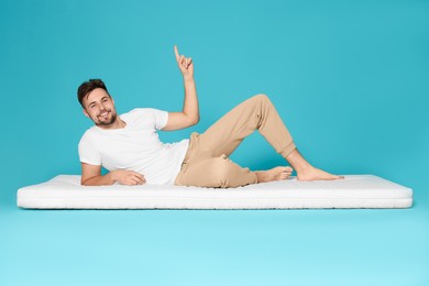 Man on soft mattress pointing upwards against light blue background