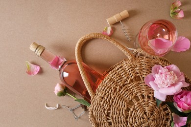 Flat lay composition with rose wine, wicker bag and beautiful pink peonies on brown background