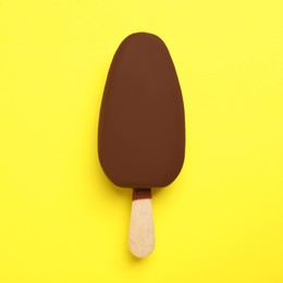 Photo of Ice cream glazed in chocolate on yellow background, top view