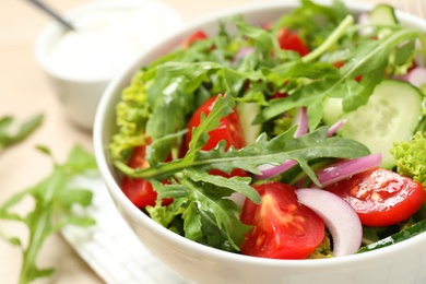 Delicious salad with arugula and vegetables in bowl, closeup