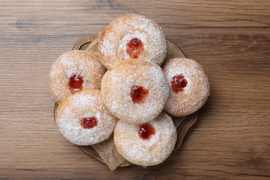 Delicious donuts with jelly and powdered sugar on wooden table, top view