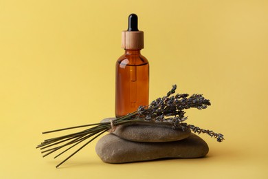 Bottle of face serum, spa stones and lavender flowers on yellow background