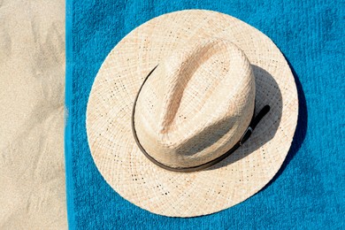 Photo of Soft blue beach towel with straw hat on sand, top view