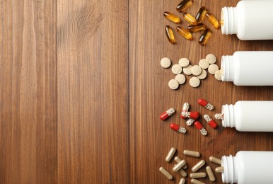 Overturned bottles with different dietary supplements on wooden table, flat lay. Space for text