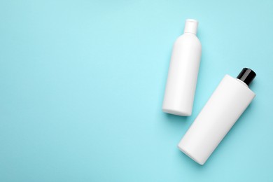 Bottles of shampoo on light blue background, flat lay. Space for text