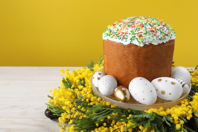 Photo of Traditional Easter cake with sprinkles, painted eggs and beautiful spring flowers on white wooden table, space for text