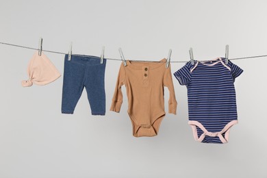 Different baby clothes drying on laundry line against light background