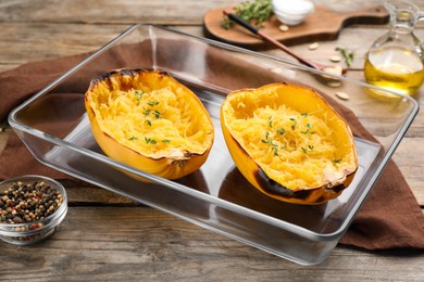 Halves of cooked spaghetti squash with thyme in baking dish on wooden table