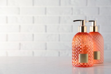 Stylish dispensers with liquid soap on wooden table near white brick wall, space for text