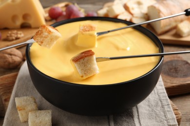 Dipping pieces of bread into tasty cheese fondue at table, closeup