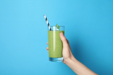 Woman holding glass of fresh green smoothie on light blue background, closeup