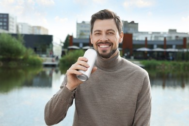 Photo of Happy man holding tin can with beverage near river outdoors