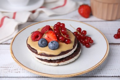 Crunchy rice cakes with peanut butter and sweet berries served on white wooden table, closeup