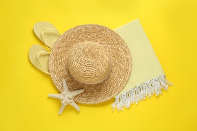 Beach towel, flip flops and straw hat on yellow background, flat lay