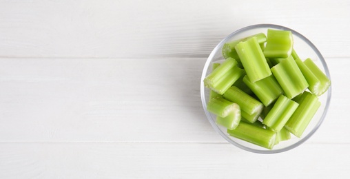 Photo of Cut celery in glass bowl on white wooden table, top view. Space for text