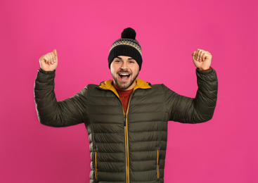 Happy young man in warm clothes on pink background. Winter vacation