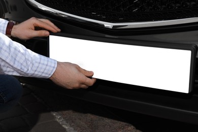 Man installing vehicle registration plate outdoors, closeup. Mockup for design