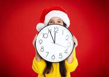 Girl in Santa hat with clock on red background. New Year countdown