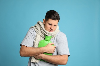 Ill man with hot water bottle suffering from cold on light blue background