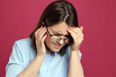Young woman suffering from migraine on crimson background