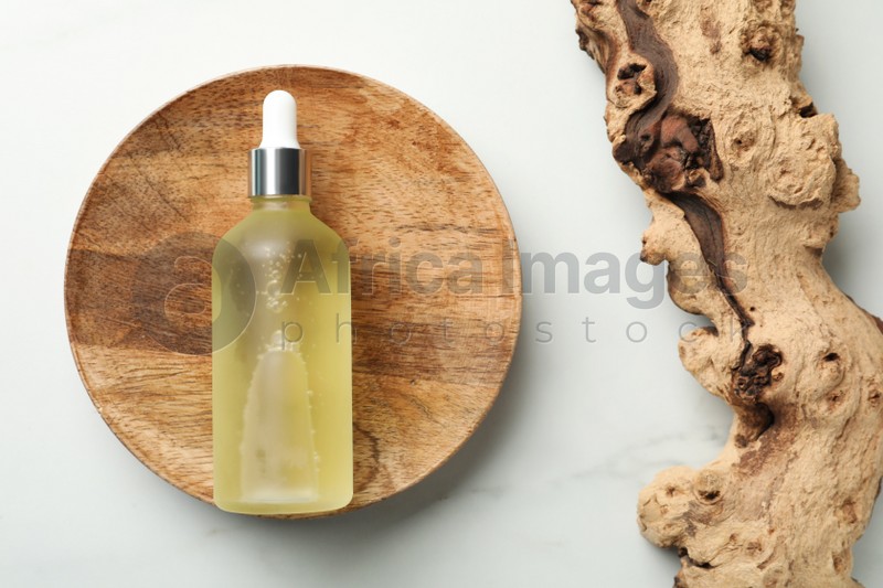 Wooden plate with bottle of hydrophilic oil near tree bark on white background, flat lay