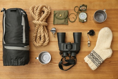 Flat lay composition with sleeping bag and camping equipment on wooden background