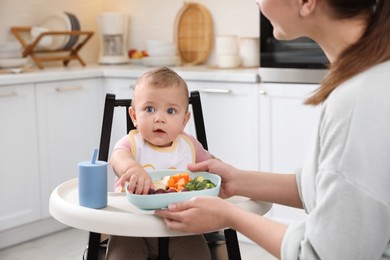 Mother feeding her cute little baby in kitchen