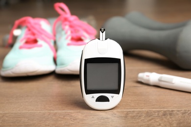 Digital glucometer, dumbbells and sneakers on wooden background. Diabetes concept