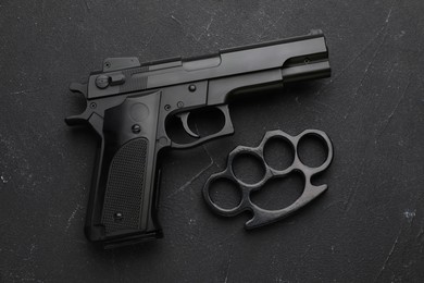 Brass knuckles and gun on black stone background, flat lay
